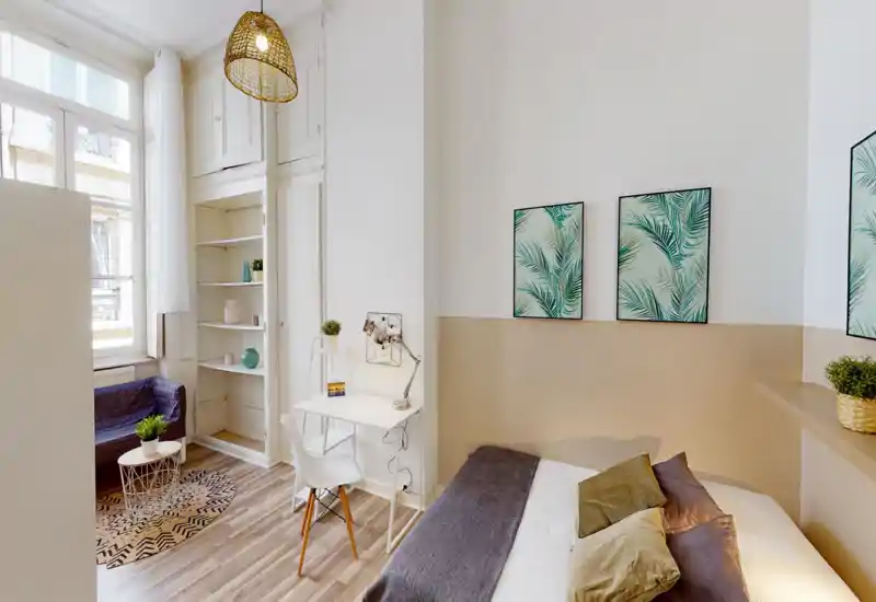 Bright, well-staged bedroom with a comfortable double bed, cozy pillows and tasteful botanical wall art. The room features a small workspace, natural light from a large window and coordinated neutral tones.