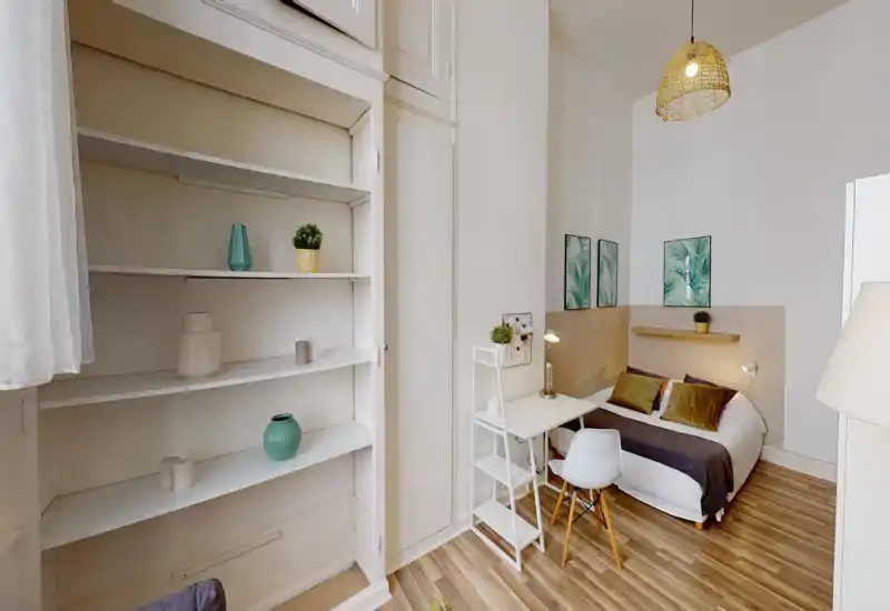 Bright, styled bedroom with a double bed, bedside lamps and decorative cushions; a small desk and shelving create a practical, cozy corner ideal for a short-term rental.