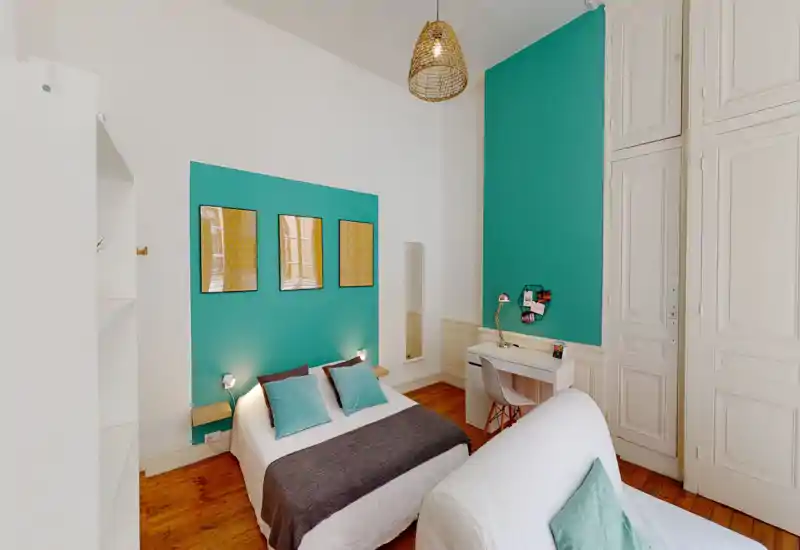 Bright, stylish bedroom with a double bed, teal accent wall, bedside lamps and a small desk. Warm wooden floors and tasteful cushions create a welcoming atmosphere.