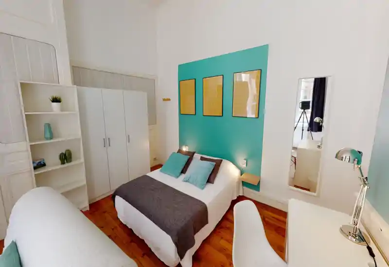 Bright, stylish bedroom with a centrally placed double bed, teal accent wall and coordinated cushions. The room features wooden floors, bedside lighting, a wardrobe and a small desk — ideal for short-term rentals.