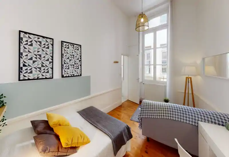 Bright, modern bedroom with a comfortable double bed, decorative pillows and a warm wooden floor. Large window floods the room with natural light and tasteful framed artwork adds a contemporary touch.