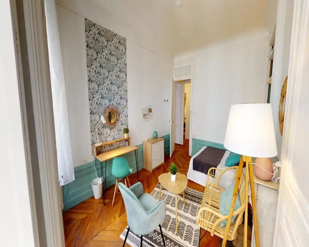 Bright, well-staged bedroom corner with a visible single bed, cozy seating area, patterned accent wall and a small desk — ideal for a comfortable city rental.