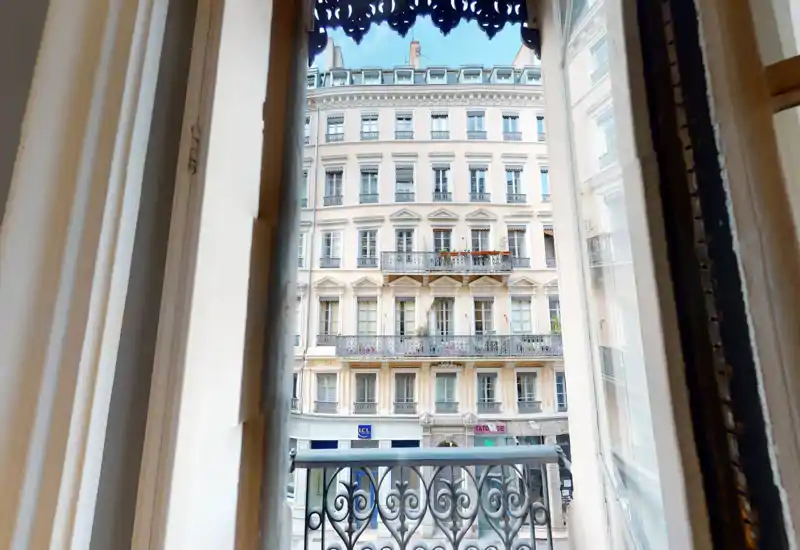 Piccola vista da balcone su una facciata urbana classica con ringhiere ornate — luce diurna brillante e finestre rivolte sulla strada.