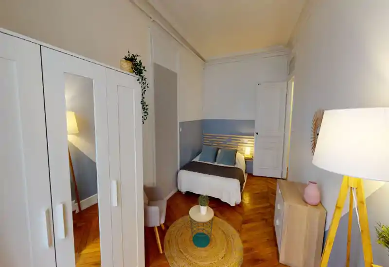 Camera da letto luminosa e accogliente con letto matrimoniale, dettagli blu e pavimenti in legno caldi. La stanza è ben arredata con lampade da comodino, tappeto e mobili contenitori, perfetta per annunci.