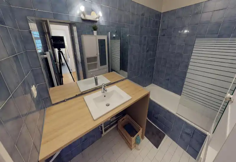 Clean, well-lit bathroom with a sink set in a wooden countertop, tiled walls and a bath with a partial glass screen.