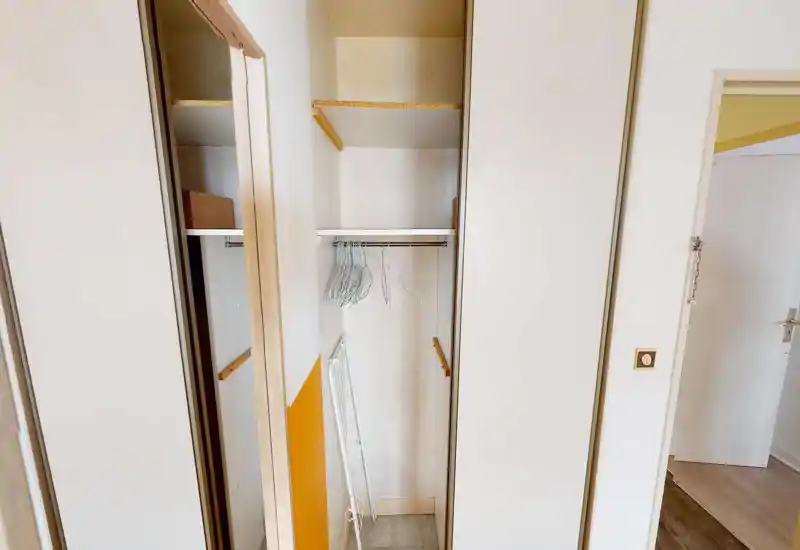 Petit placard encastré/zone de rangement d’entrée avec tringle et plusieurs cintres métalliques. Espace simple et propre, adapté aux manteaux ou au rangement léger.