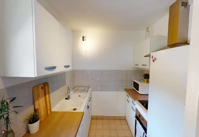 Cucina compatta e ordinata con piani in effetto legno, pensili bianchi, lavello e elettrodomestici integrati — spazio luminoso e funzionale ideale per un piccolo appartamento.