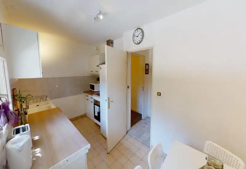 Cuisine compacte et bien rangée avec plan de travail en bois, évier, plaque de cuisson et petit coin repas. Espace lumineux et fonctionnel avec rangements simples et petites plantes décoratives.