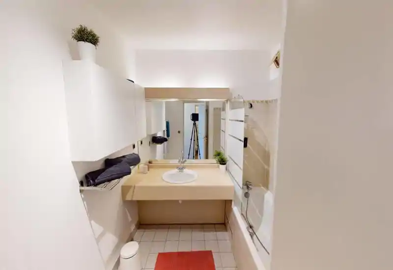 Salle de bain lumineuse et moderne avec lavabo sur meuble, grand miroir et baignoire-douche. Carrelage neutre et lignes épurées pour une impression propre et fraîche.