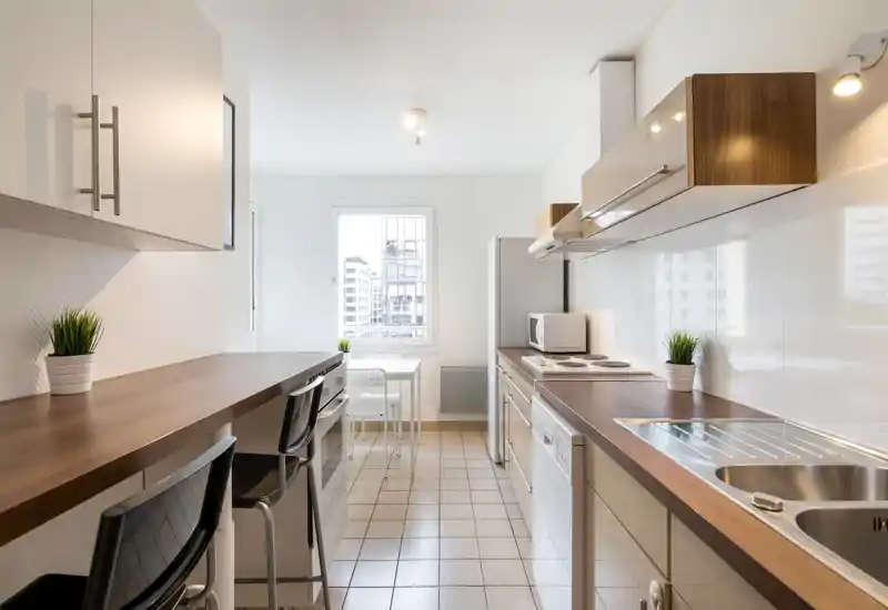 Bright, modern galley kitchen with wooden countertops, integrated appliances and a small dining nook by the window — clean design and natural light make it ideal for compact urban living.