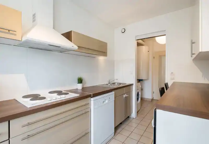 Bright, modern galley kitchen with wood-effect countertops, built-in electric hob, dishwasher and double sink; compact utility area with washer visible through the doorway.