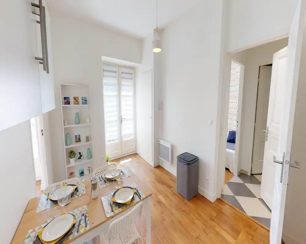 Área de comedor moderna y luminosa con mesa puesta para cuatro, suelos de madera y una puerta de cristal que aporta luz natural — ideal para comidas y reuniones.