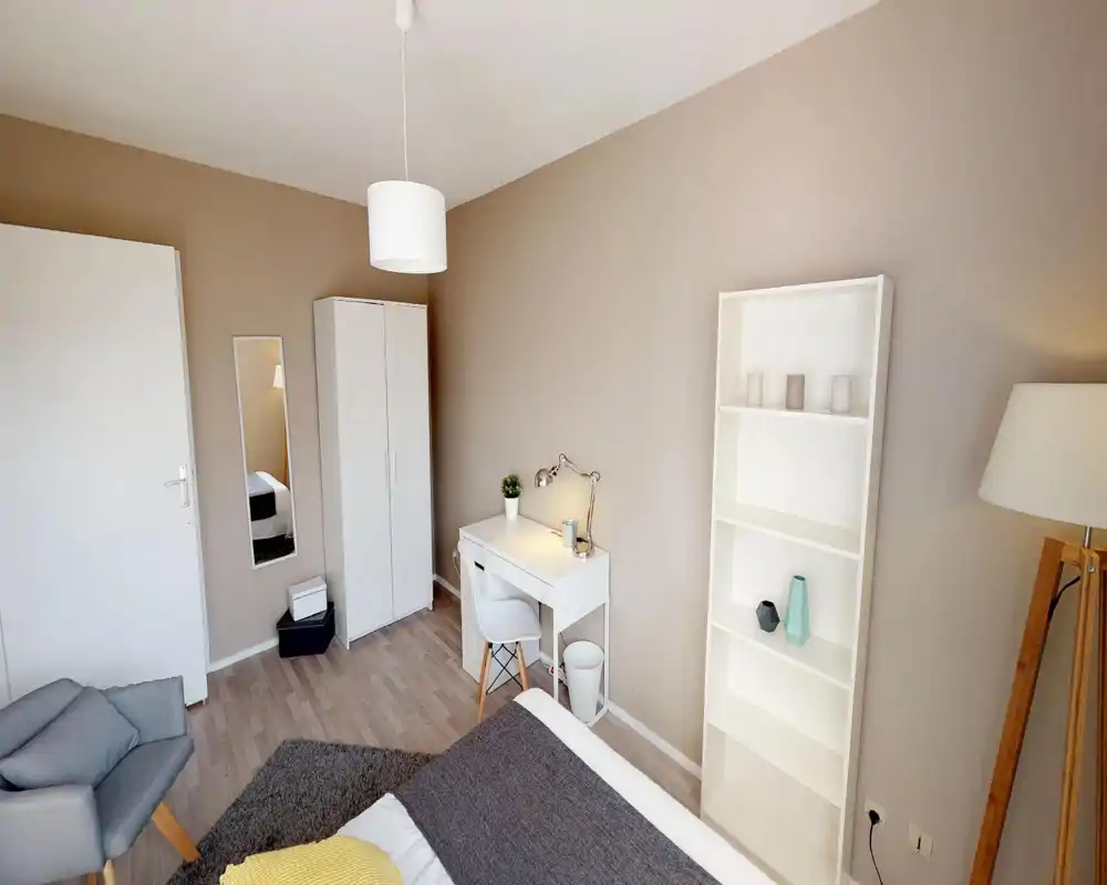 Camera da letto luminosa e ben allestita con letto visibile, scrivania, armadio e scaffale — toni neutri e dettagli accoglienti per un ambiente tranquillo.