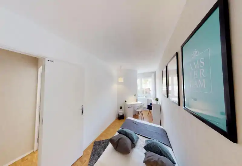 Sunny, neatly staged bedroom with a visible double bed, decorative cushions, a rug and a small desk by the window — bright and inviting for guests.