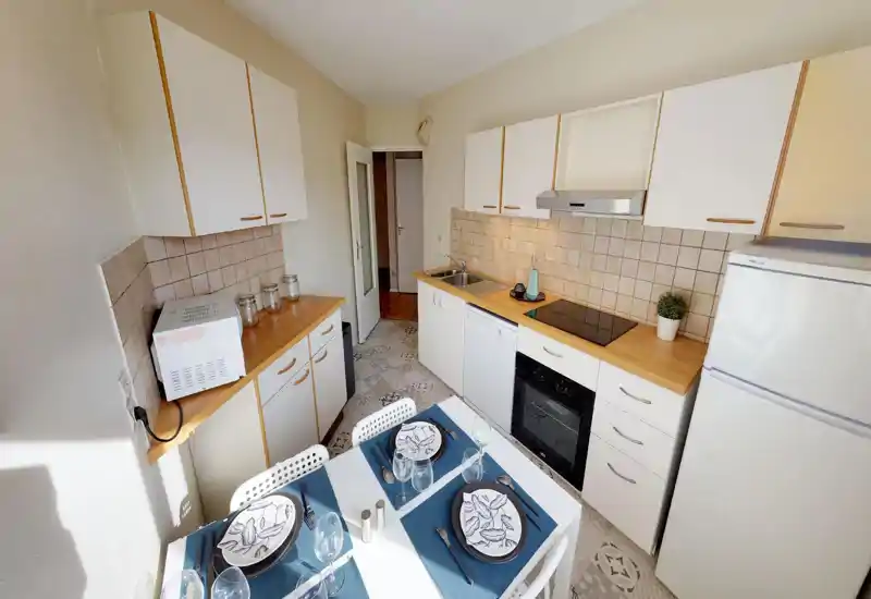Bright, compact kitchen with white cabinets, wooden countertops, electric cooktop and a set table for four; well lit and neatly staged for rental photos.