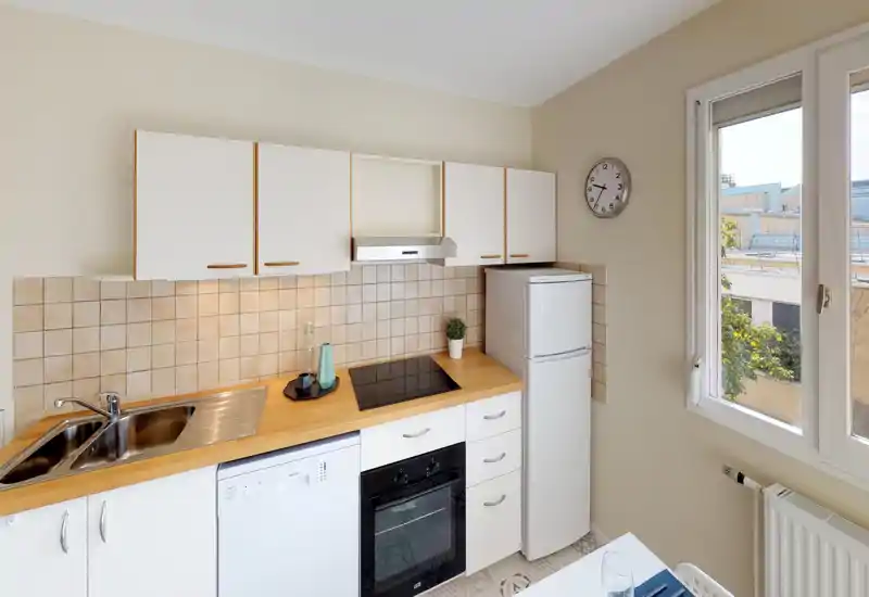 Bright, compact modern kitchen with wooden countertops, tiled backsplash, built-in oven and induction hob; window provides natural light and a small fridge completes the layout.