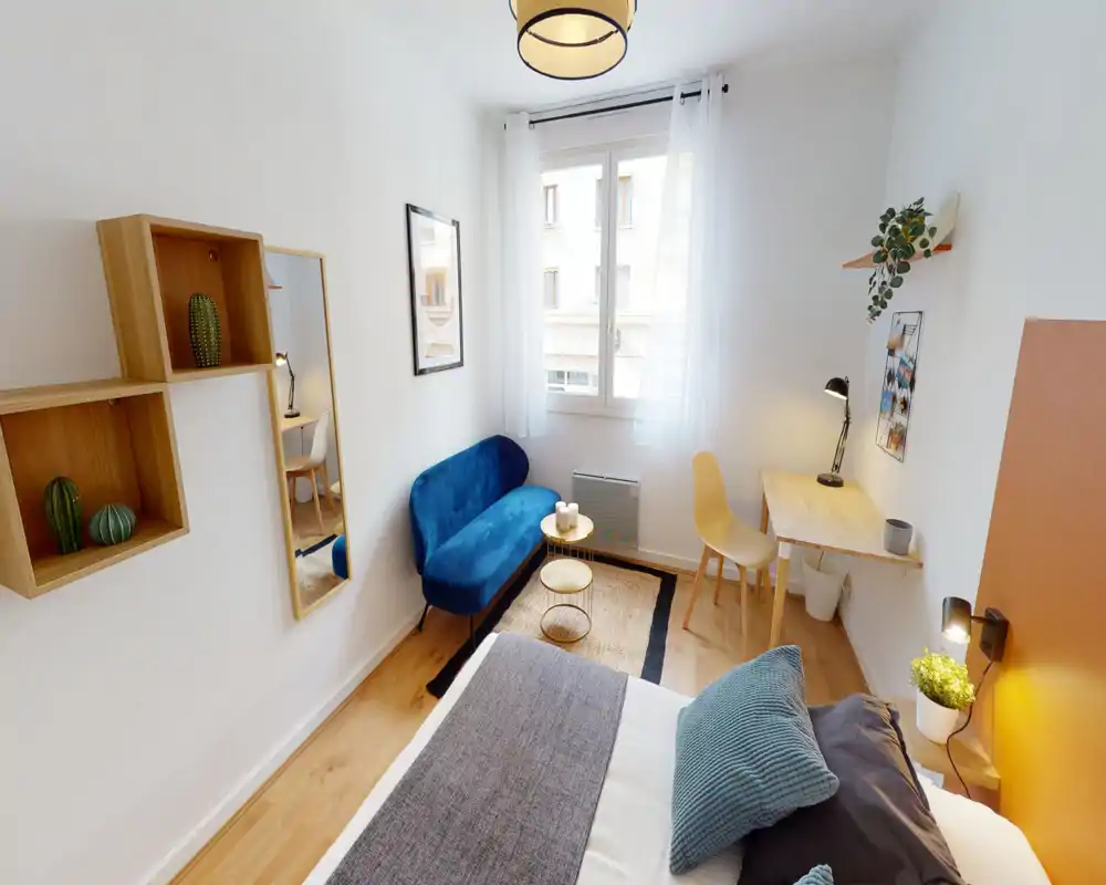 Bright, stylish bedroom with a comfortable double bed in the foreground, a blue loveseat by the window, and a small desk—ideal for work-and-relax stays.