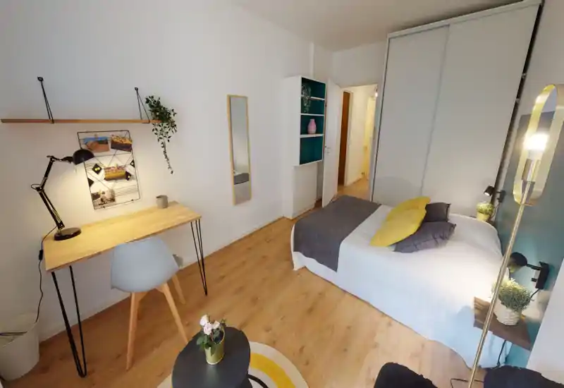 Camera da letto luminosa e ben arredata con letto comodo, tessili accoglienti e una piccola scrivania. Pareti neutre, pavimento in legno e dettagli curati per un’atmosfera moderna e invitante.