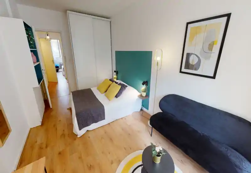 Camera da letto elegante e compatta con un comodo letto matrimoniale, cuscini coordinati e un'area salotto accogliente. Arredamento moderno e luminoso con pavimento in legno e armadio a muro.