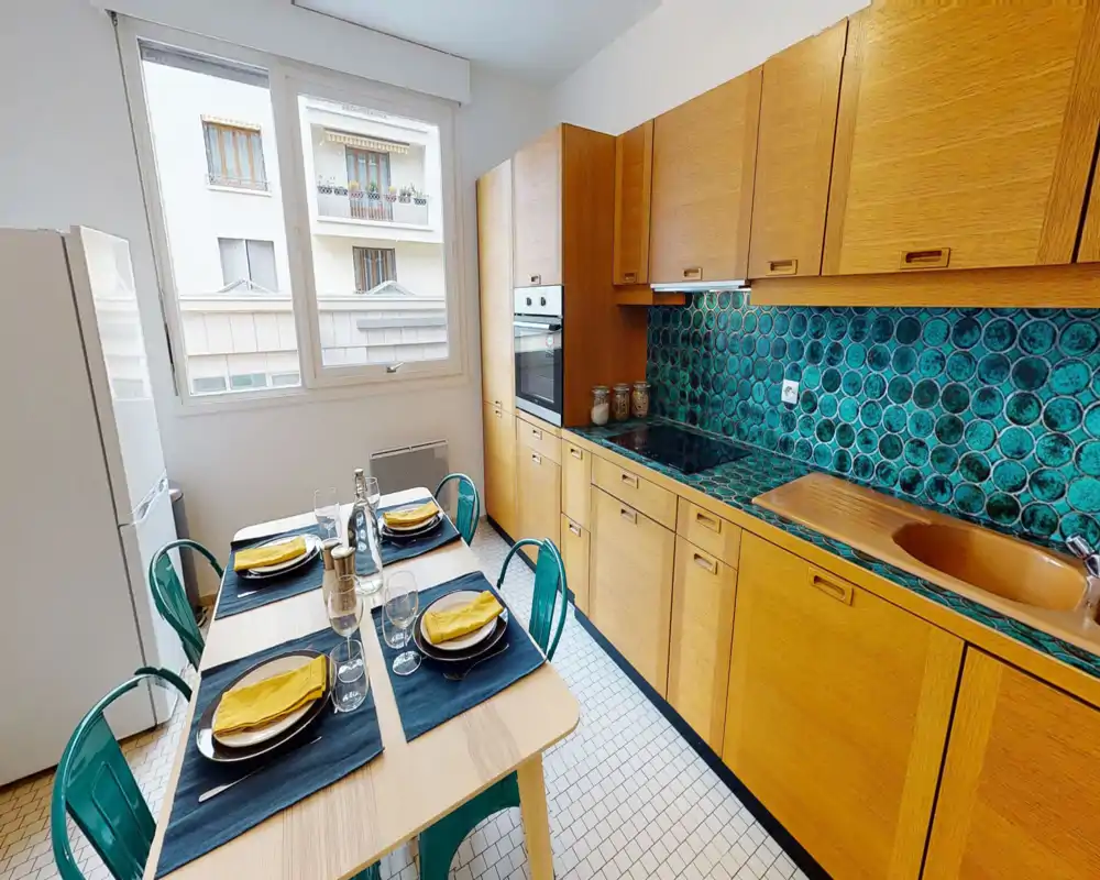 Bright, well-equipped kitchen with wooden cabinets, turquoise tiled backsplash and a dining table set for four — ideal for comfortable meals and social cooking.