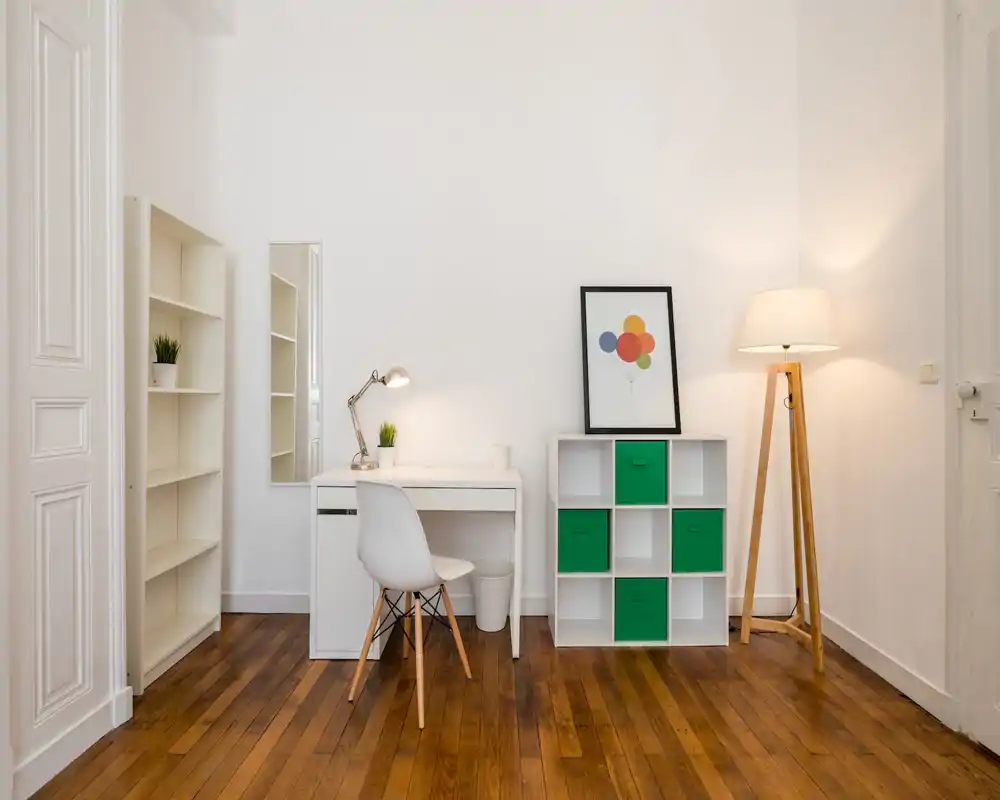 Bright, minimal home office corner with a white desk, modern chair, shelving and a standing lamp — a clean and functional workspace.