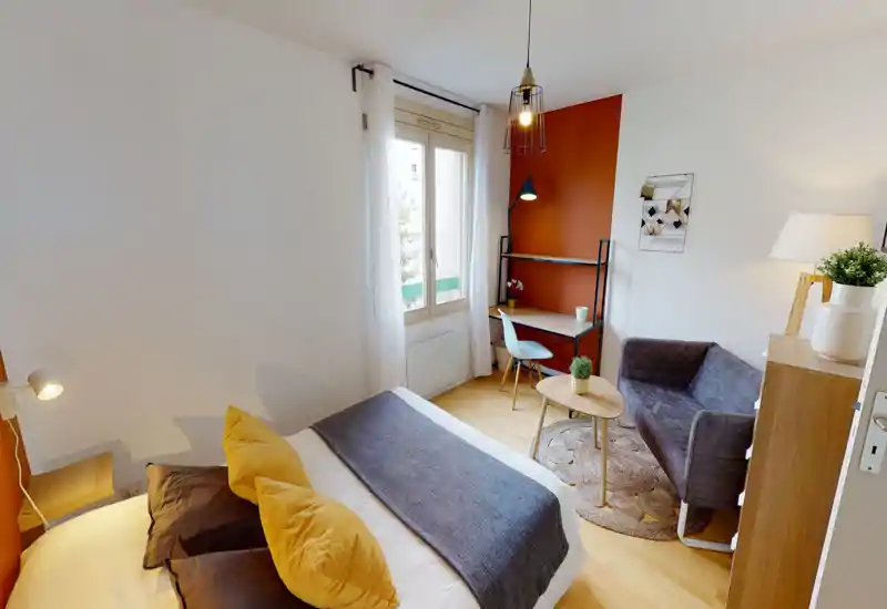 Bright, cozy bedroom with a double bed, decorative cushions and a small seating area. Natural light from the window and a stylish accent wall create a warm, modern atmosphere — ideal for rental photos.