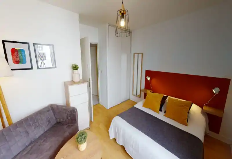 Bright, well-staged bedroom with a double bed dressed in white linens and mustard cushions, a cozy sofa and wooden details creating a warm, inviting atmosphere.