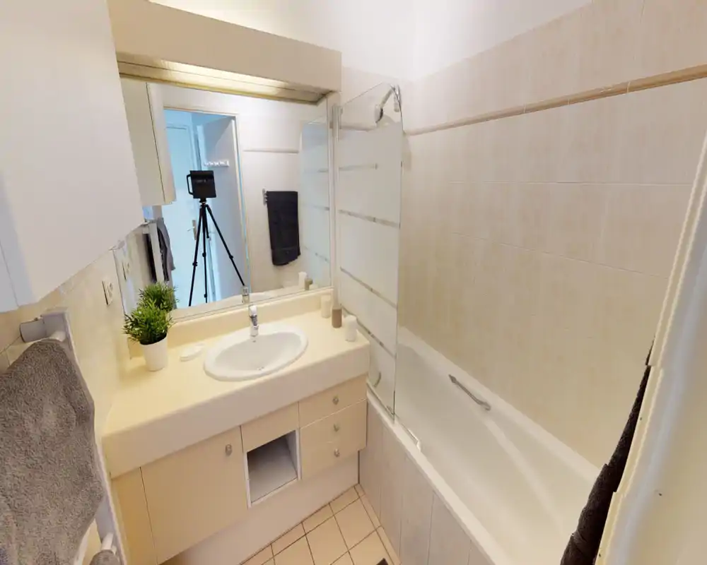 Bright, tidy bathroom with a bathtub and integrated sink. Neutral tiles and a large mirror create a clean, functional space ideal for rental listings.