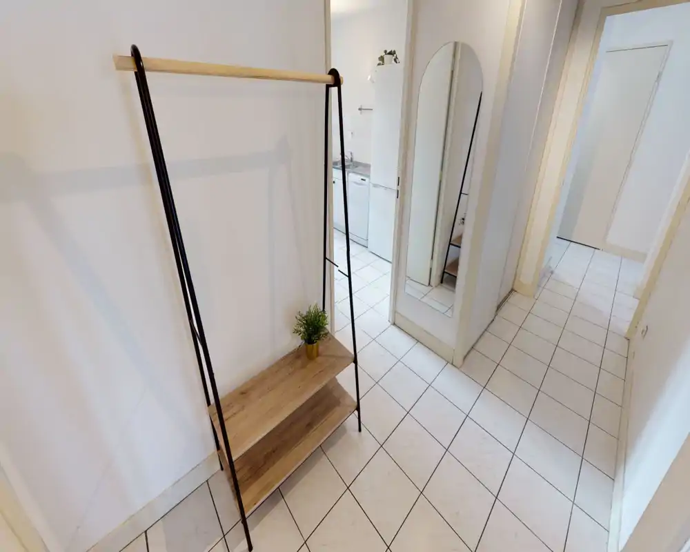 Bright, tiled entrance/hallway with a freestanding clothing rack and full-length mirror, leading to the kitchen and interior doors.