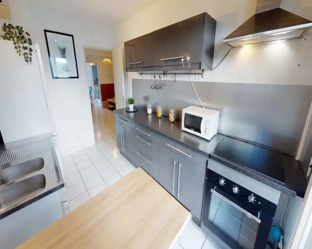 Modern galley kitchen with glossy dark cabinets, built-in oven and stovetop, microwave on the counter and a stainless sink; bright tiled floor and clean, functional layout ideal for a rental.