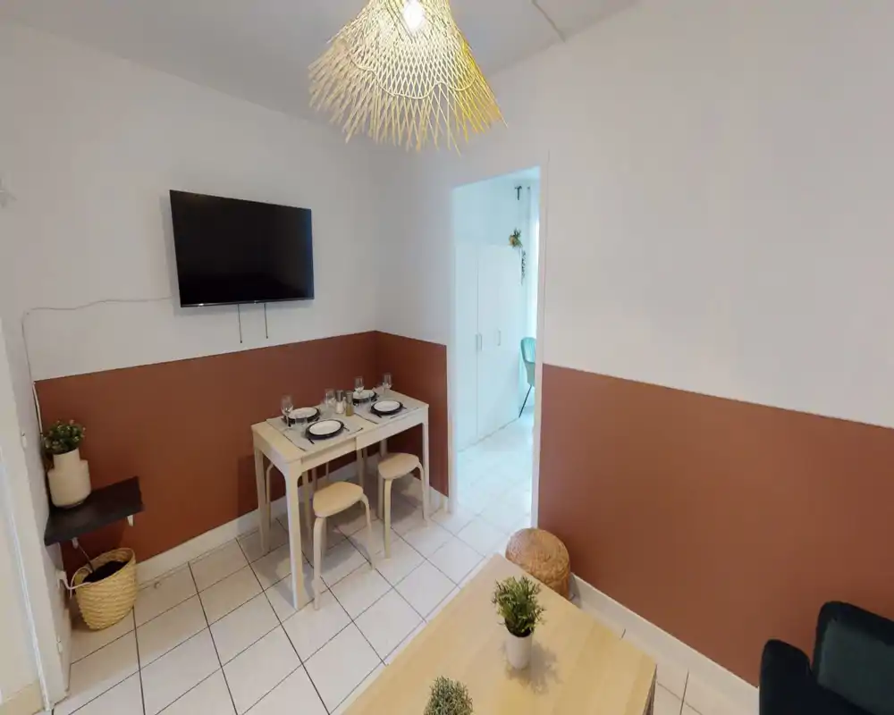 Small staged dining area with a two-tone wall, wall-mounted TV and a compact table set for four — bright, cozy and well arranged for a city apartment.