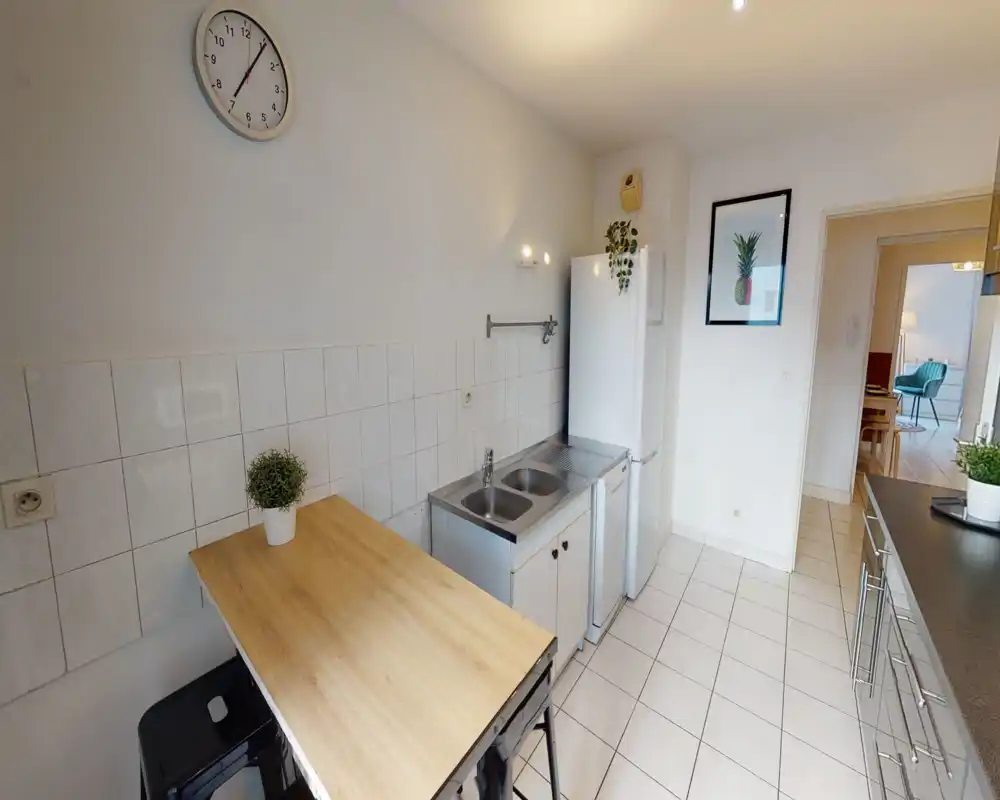 Bright, tidy kitchen with a double stainless sink, full-height refrigerator and a wooden breakfast bar; minimal, modern décor and a clean tiled floor.