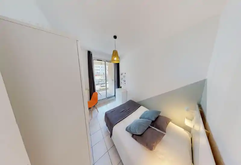 Bright, well-staged bedroom with a double bed, decorative cushions and a warm bedside light; sliding doors open to a balcony providing natural light.