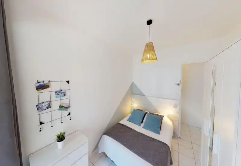 Bright, neatly styled bedroom with a double bed, coordinating blue cushions and a woven pendant lamp; white walls and tiled floor create a fresh, minimalist feel.