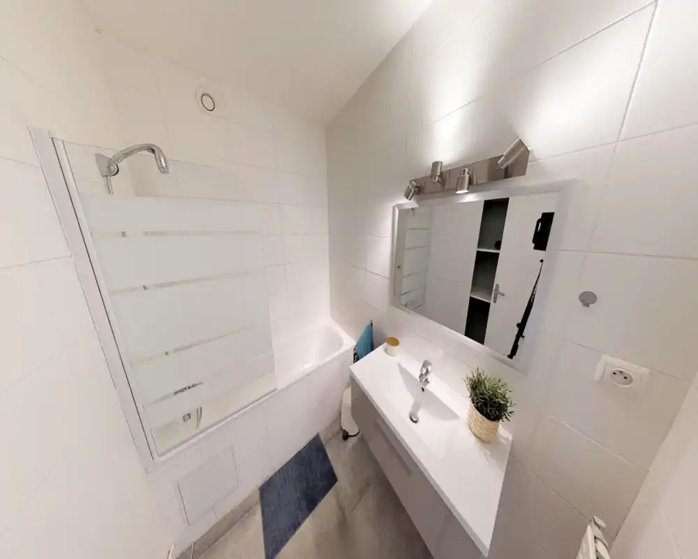 Bagno moderno e compatto con vasca/doccia, piastrelle bianche, mobile lavabo con specchio e illuminazione chiara e pulita.