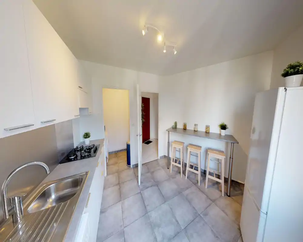 Cucina moderna e luminosa con piano di lavoro lungo, lavello e piano cottura a gas, più un bancone con tre sgabelli — stile minimal e disposizione funzionale.