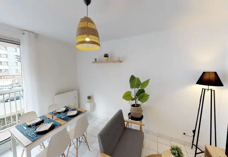 Espace repas moderne et lumineux avec une table dressée pour quatre, accents en bois clair et éléments décoratifs chaleureux comme des plantes et un éclairage ambiant.