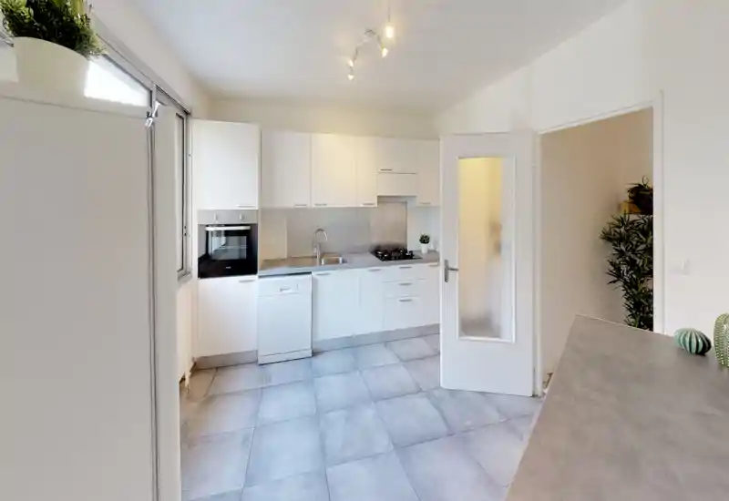Cuisine moderne et lumineuse avec éléments blancs, four encastré, plaque à gaz et lave-vaisselle. Sol carrelé et style minimaliste pour un espace de cuisson fonctionnel.