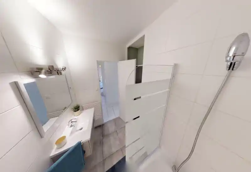 Salle de bain moderne et propre avec douche à l'italienne, carreaux blancs, lavabo avec miroir et éclairage contemporain — lumineuse et bien entretenue.