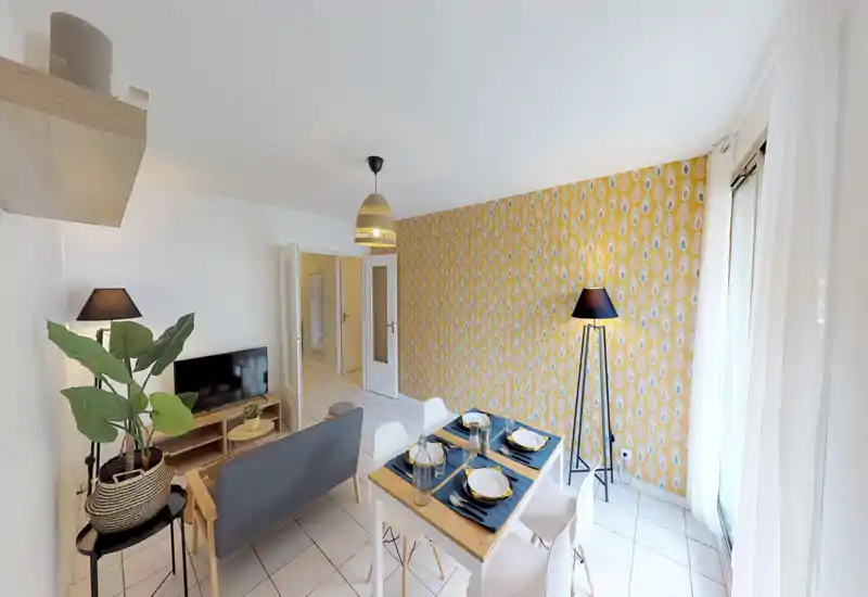 Bright, styled living room with a small sofa, TV, dining table set for four and a patterned accent wall; large window provides abundant natural light.