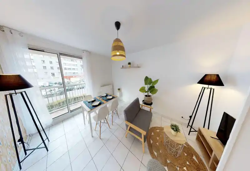 Séjour moderne et lumineux avec un canapé deux places, une table à manger pour quatre, un éclairage soigné et une grande baie vitrée donnant sur un balcon — idéal pour recevoir et dîner.