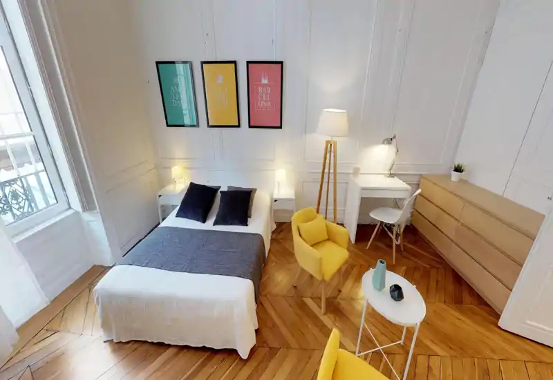 Bright, stylish bedroom with a centrally placed double bed, decorative cushions, wood parquet flooring and a small workspace — ideal for short-term rentals.