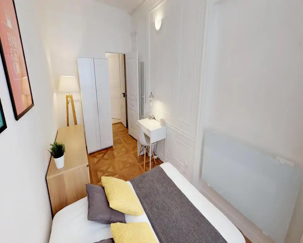 Chambre lumineuse et aérée avec lit bien fait, coussins décoratifs et petit bureau contre le mur — idéale pour une personne seule ou un couple.