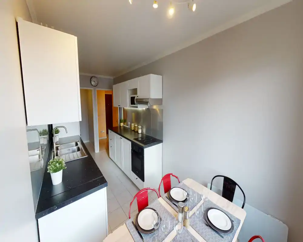 Modern, compact fitted kitchen with white cabinets, black countertops, built-in oven and a cozy dining table set for four — bright and practical for everyday use.
