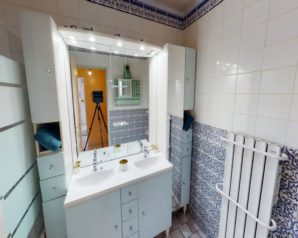 Bright, well-organized bathroom with a double sink vanity, mirrored cabinet and decorative blue patterned tiles.