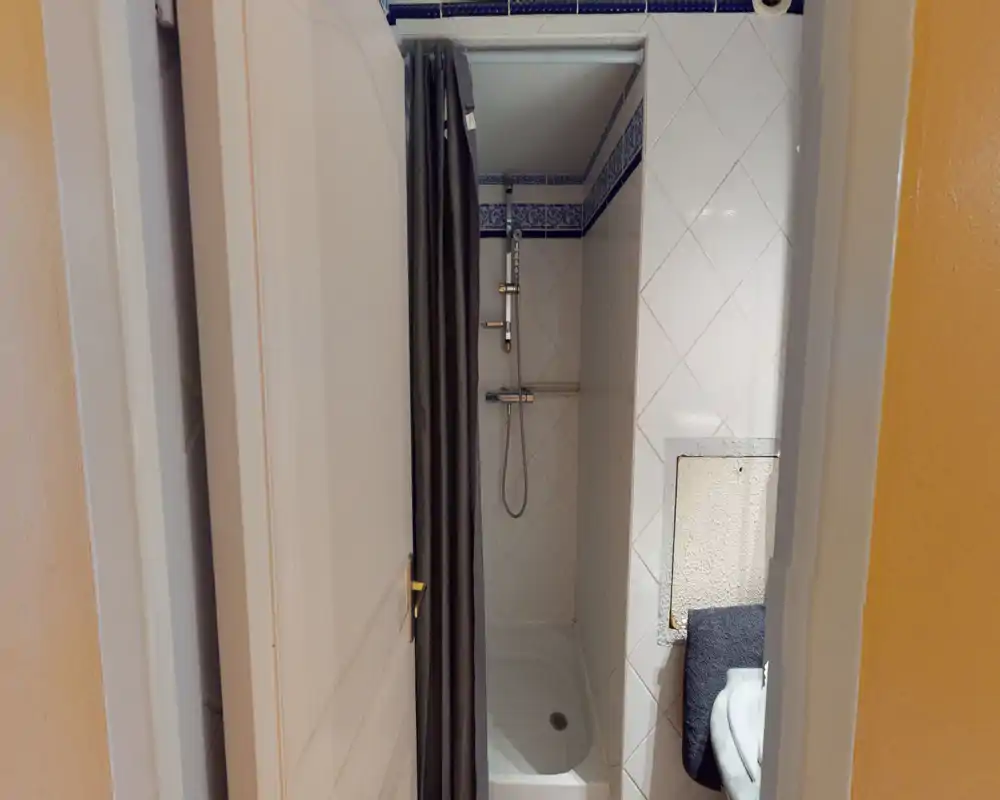 Compact tiled bathroom with a shower stall, overhead mixer and a dark shower curtain; neat, well-lit space suitable for short-stay rentals.