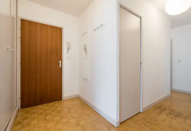Entrée d'appartement lumineuse et minimaliste avec porte en bois, parquet et patères murales. Lignes épurées et tons neutres offrent une première impression accueillante.