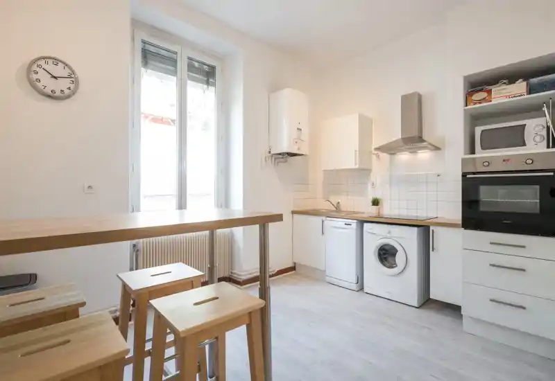 Bright modern kitchen with white cabinets, wooden countertops and bar seating; includes dishwasher, washing machine and built-in oven — ideal for functional city living.