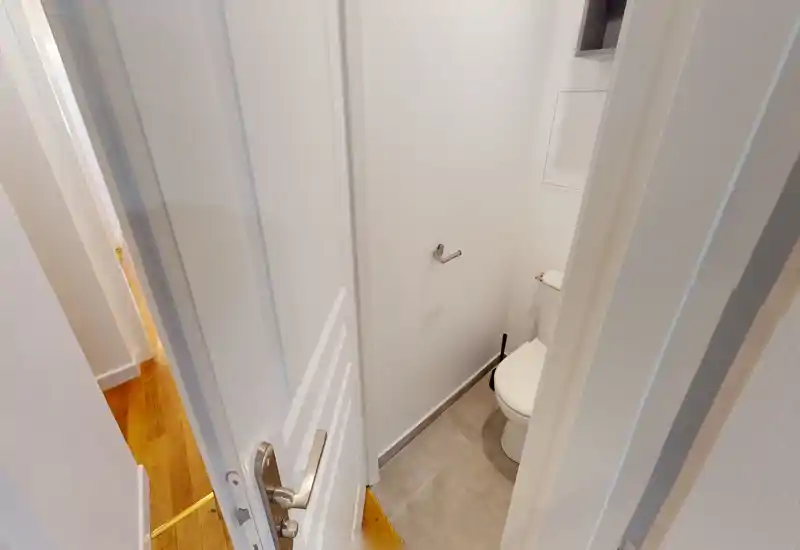 Petit WC d'appoint avec toilette blanche, sol carrelé et murs blancs propres — une petite salle d'eau bien éclairée, parfaite comme cabinet de toilette.