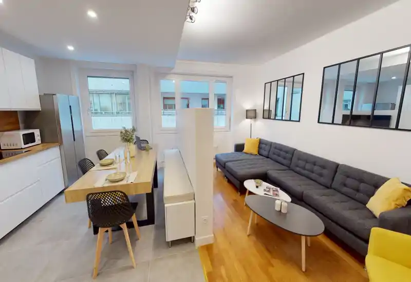 Espace de vie contemporain en open-space avec un grand canapé d'angle gris, une table basse et un comptoir repas qui relie la cuisine au salon. De larges fenêtres et une décoration soignée créent une ambiance lumineuse et accueillante, parfaite pour se détendre et recevoir.